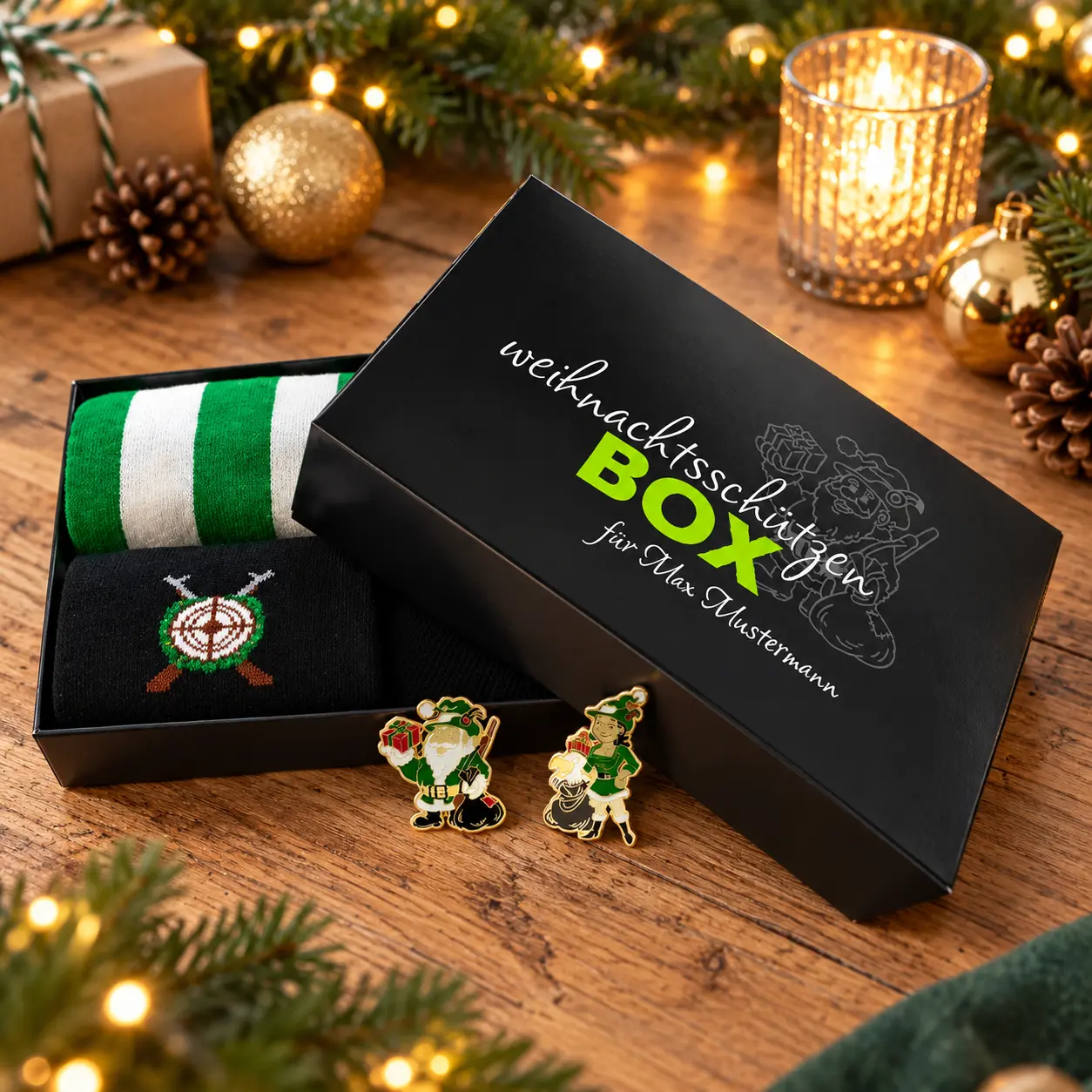 Geöffnete schwarze Weihnachtsschützen-Box mit grün-weiß gestreiften und schwarzen Textilien mit Zielscheibenmotiv. Daneben zwei Figuren-Anstecker. Der beschriftete Deckel liegt schräg auf der Box, umgeben von Weihnachtsdekoration., Weihnachtsgeschenkbox,