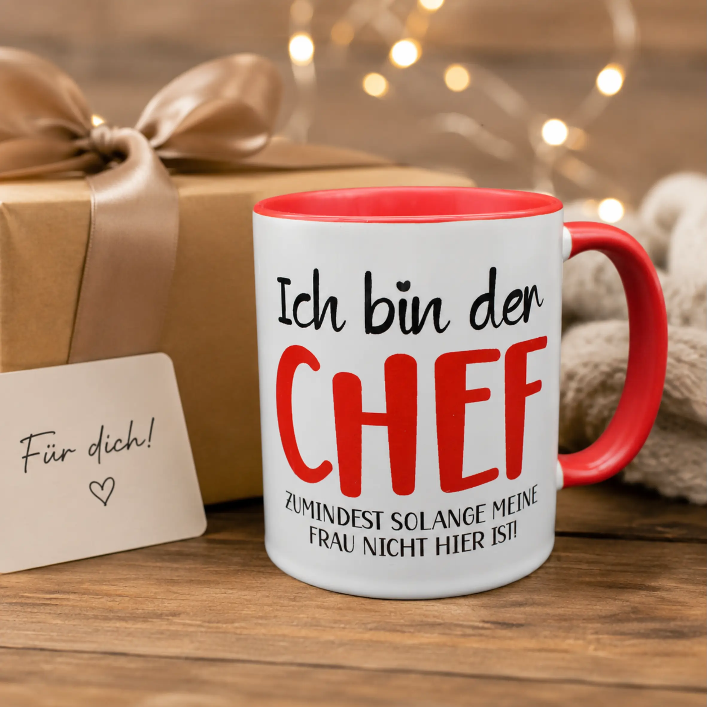 TwoTone-Tasse Ich bin der Chef mit rotem Henkel und roter Innenseite Weiße TwoTone-Tasse mit roter Innenseite und rotem Henkel, bedruckt mit dem Spruch „Ich bin der Chef, zumindest solange meine Frau nicht hier ist“. Daneben stehen ein Geschenk und eine kleine Karte.