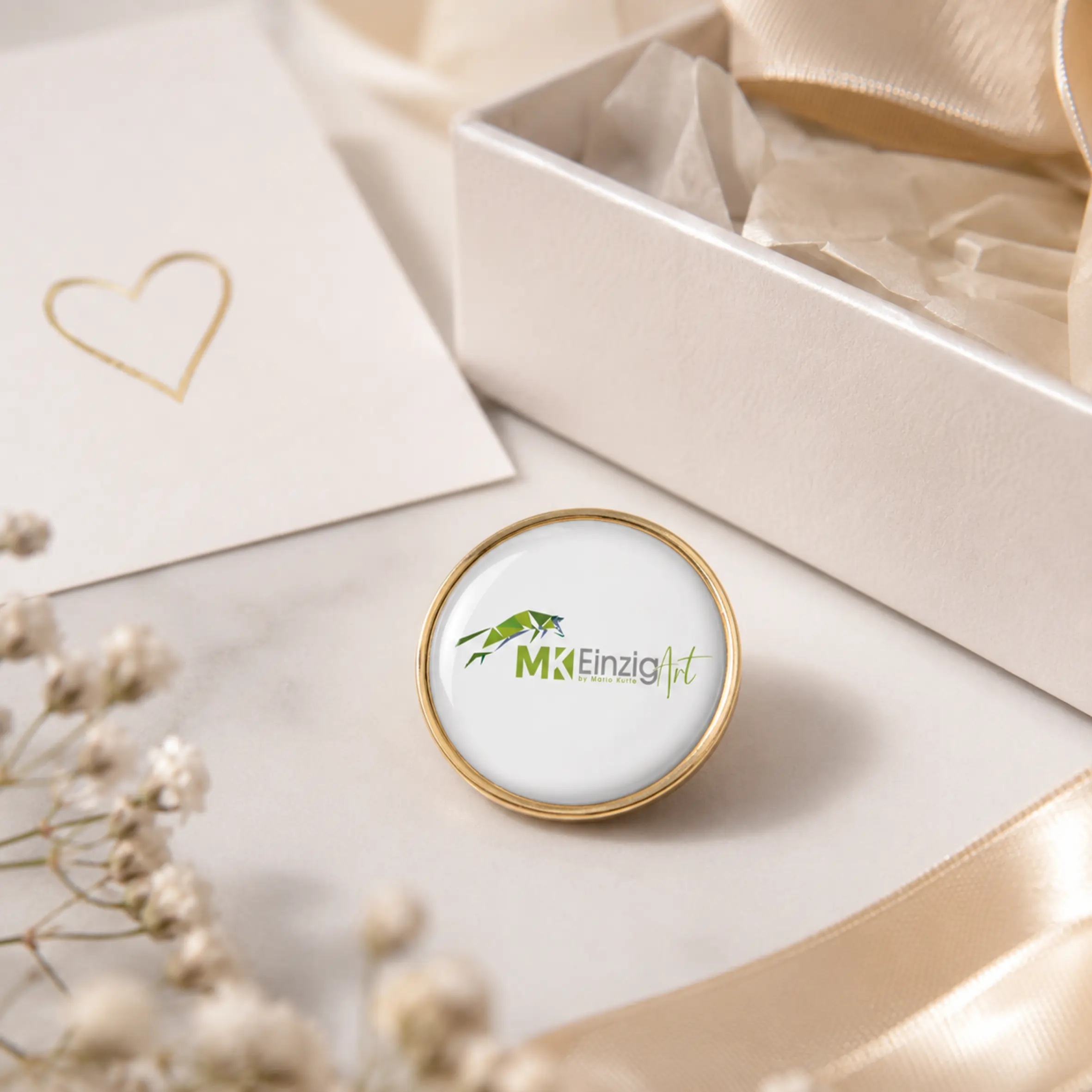 Rundes Expressabzeichen in Goldoptik mit weißer, gewölbter Motivfläche und individuellem Logo im Zentrum, dekorativ auf einer Geschenkverpackung platziert.