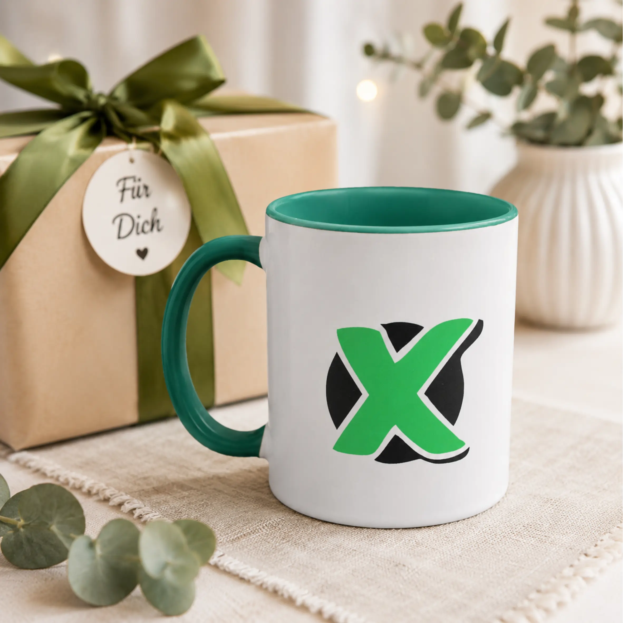 Weiße Tasse lass mich kurz überlegen mit grünem Henkel und grüner Innenseite, bedruckt mit einem großen grünen X auf schwarzem Hintergrund.