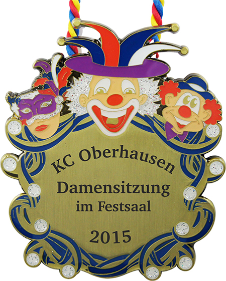 Karnevalsorden „Schild mit Luftschlangen“ mit bronzefarbenem Schild, blauen Verzierungen, drei bunten Karnevalsgesichtern und rot-gelb-blauer Kordel. Aufdruck: „KC Oberhausen Damensitzung im Festsaal 2015“., Karnevalsschmuck, Hänger, Clownenmotiv, Festzel