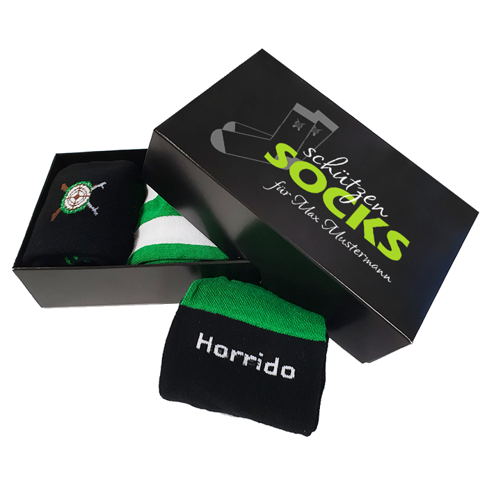 Schützensocken in schwarzer Geschenkbox mit personalisiertem Aufdruck Schwarze Geschenkbox für Schützensocken mit aufgedrucktem Schützensocken-Motiv und persönlichem Schriftzug. Daneben und in der geöffneten Box liegen schwarze Socken mit grünem Bund, Schriftzug und Schützenmotiv.