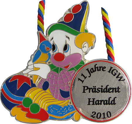Karnevalsorden „Niedlicher Clown“ mit rundem Beschriftungsfeld Silberfarbener Karnevalsorden mit bunt gestaltetem Clown, spitzem Hut und kleinem Vogel auf der Hand. Das runde Feld rechts trägt die Aufschrift „11 Jahre IGW Präsident Harald 2010“. Ein rot-gelb-blaues Band verläuft hinter dem Orden., Karnevalsorden, Clo