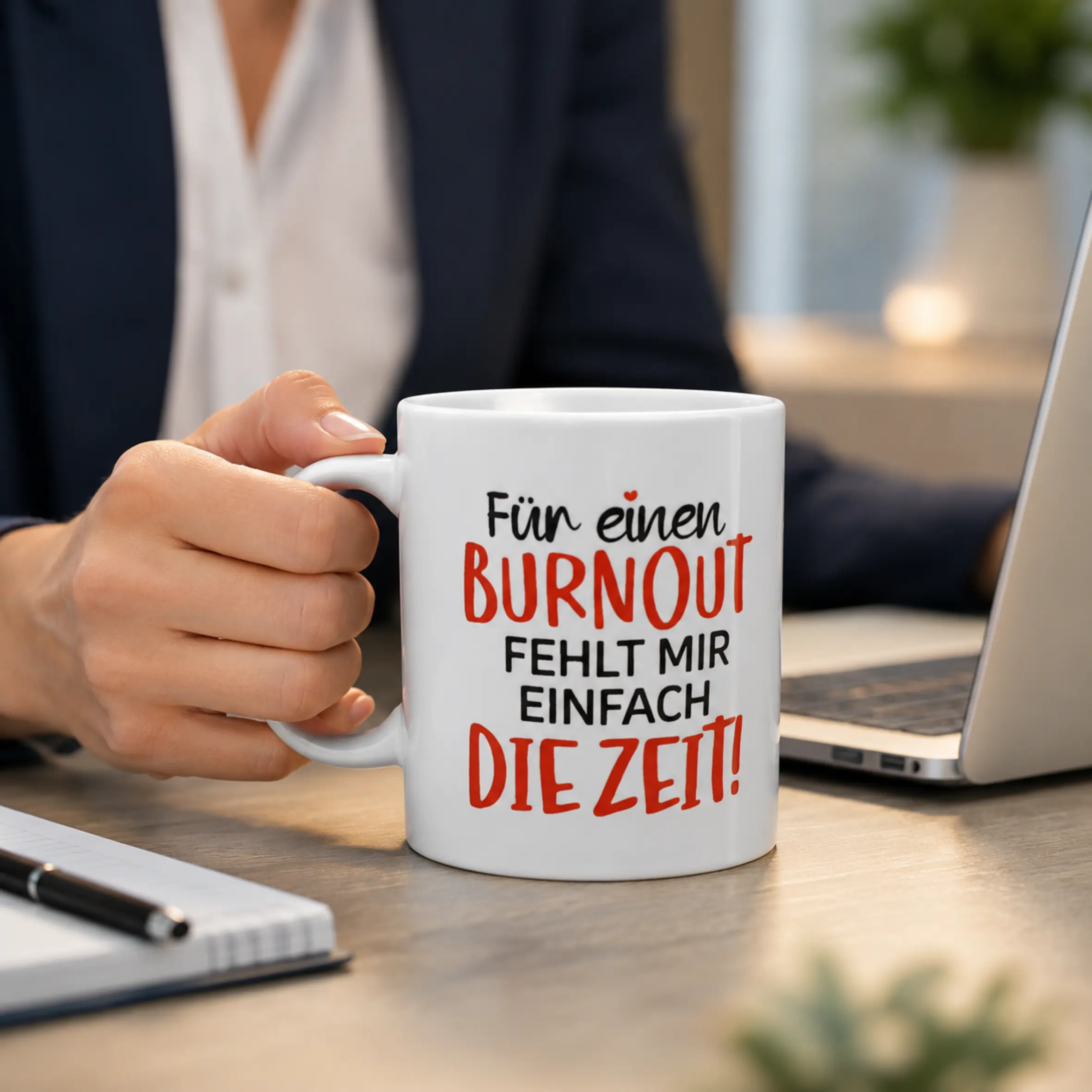 Tasse Keine Zeit für Burnout mit Spruch auf weißer Keramiktasse Weiße Tasse Keine Zeit für Burnout mit großem Spruch „Für einen Burnout fehlt mir einfach die Zeit!“ in Schwarz und Rot, auf einem Schreibtisch neben einem Laptop in der Hand gehalten.