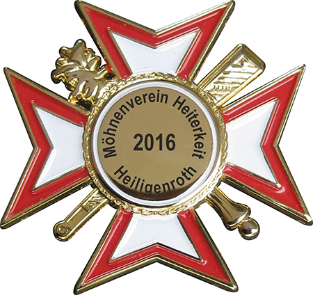 Karnevalsabzeichen rot-weiß in spitzer Form mit goldenem Mittelkreis Karnevalsabzeichen in spitzer Form mit rot-weißen Kreuzarmen, goldenem Rand und rundem Mittelkreis mit Aufdruck „Möhnenverein Hettenkelz Heiligenroth 2016“