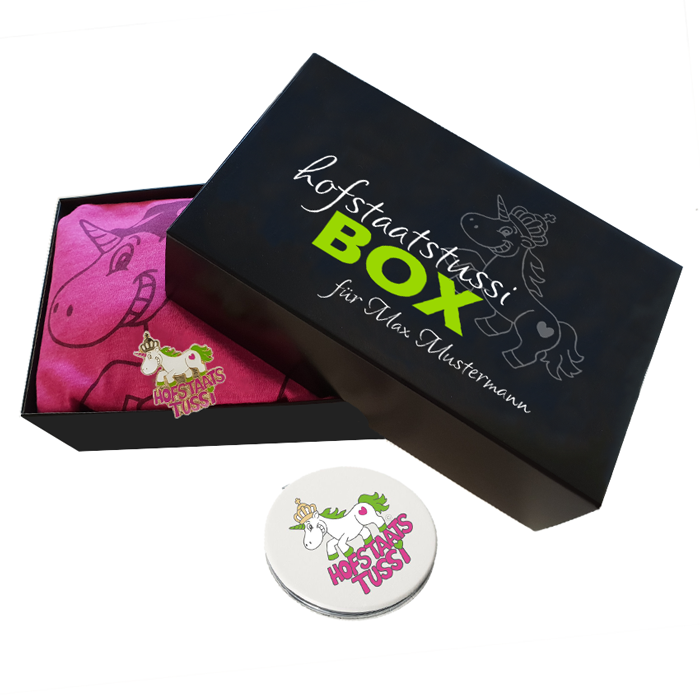 Hofstaatstussibox mit schwarzer Geschenkbox, pinkem T-Shirt, Spiegel und Abzeichen Hofstaatstussibox mit schwarzer Box und bedrucktem Deckel, darin ein pinkes Tussi-T-Shirt mit Hofstaatstussi-Motiv; davor ein runder Kosmetikspiegel und ein Hofstaatstussi-Abzeichen. Deckel mit personalisiertem Schriftzug „für Max Mustermann“.